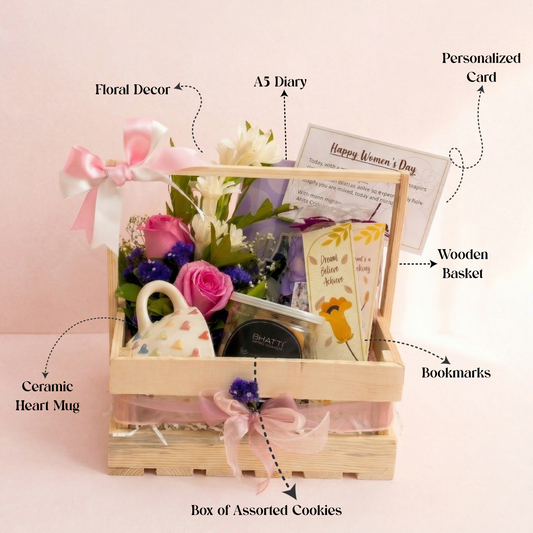Gift basket with floral decor, A5 diary, personalized card, wooden basket, ceramic heart mug, box of assorted cookies, and bookmarks on a pink background.