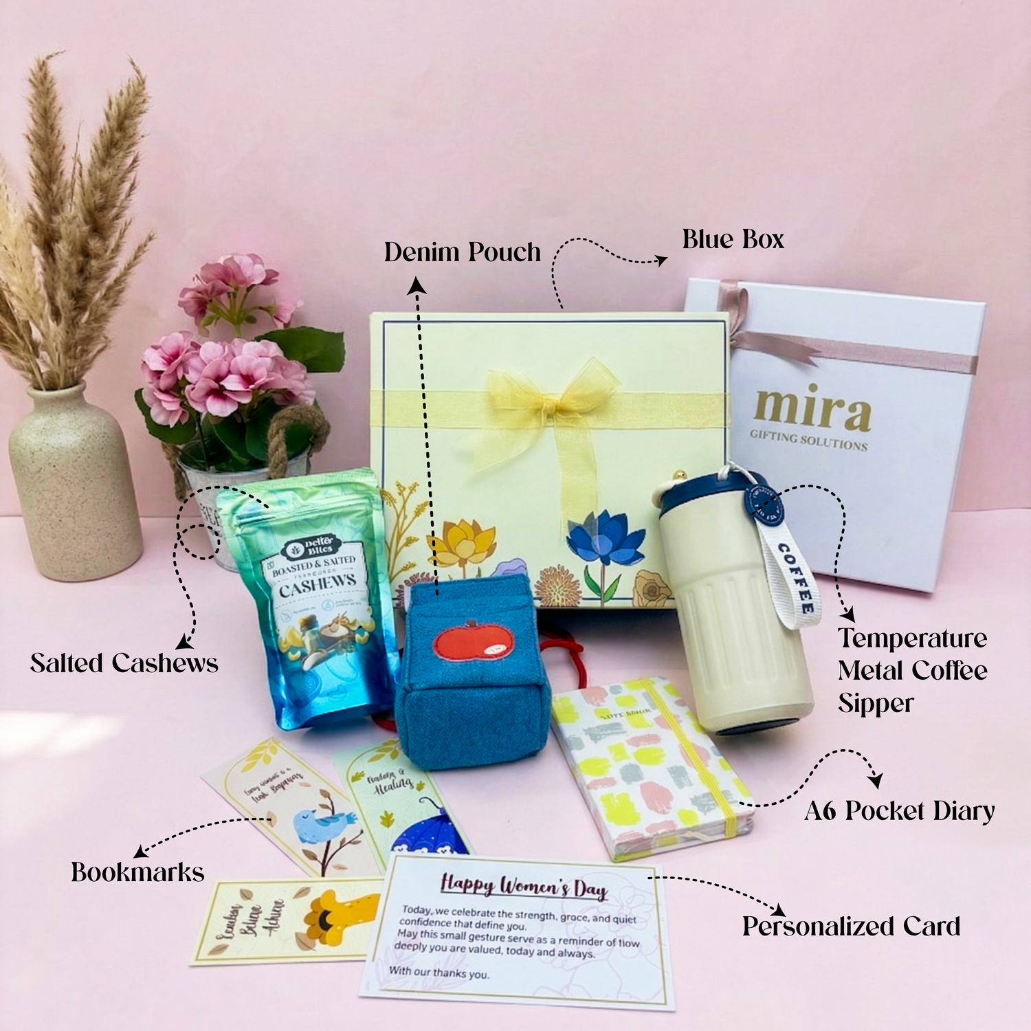 Gifting set with various items including a coffee cup, cashews, and a diary on a pink background.
