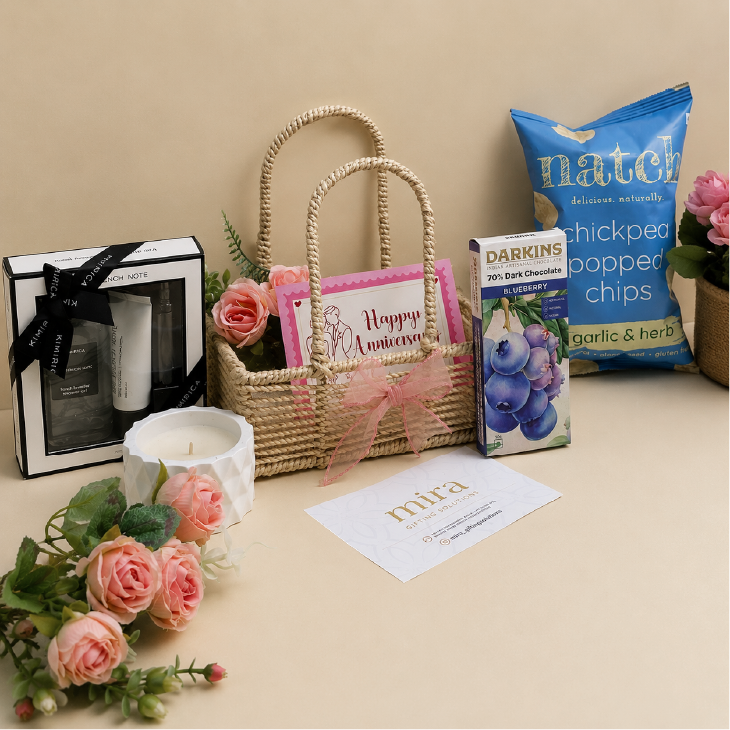Gift basket with candles, flowers, and snacks on a beige surface