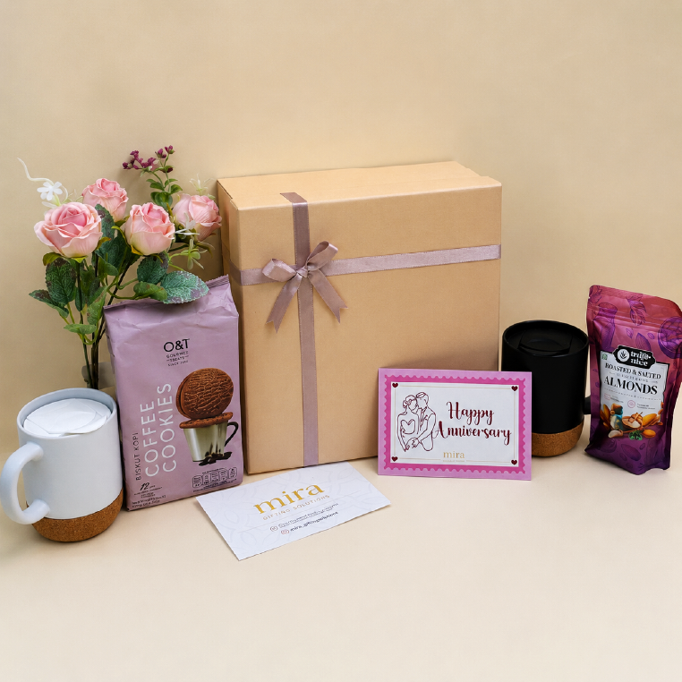 Gift box with a 'Happy Anniversary' card, cookies, coffee, and flowers on a table.
