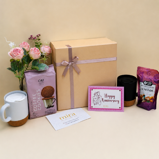Gift box with a 'Happy Anniversary' card, cookies, coffee, and flowers on a table.
