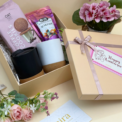 Gift set with coffee-themed items and a decorative box on a table with flowers.