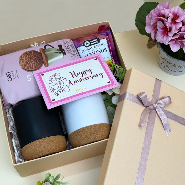 Gift box with a mug, cookies, and a card with 'Happy Anniversary' on a light surface.