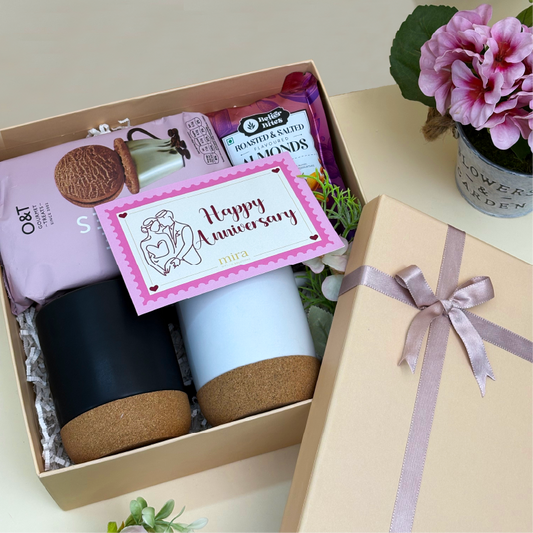Gift box with a mug, cookies, and a card with 'Happy Anniversary' on a light surface.