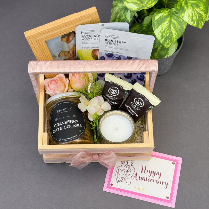 Gift basket with cookies, candles, and a card on a gray surface with a plant in the background.
