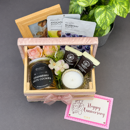 Gift basket with cookies, candles, and a card on a gray surface with a plant in the background.