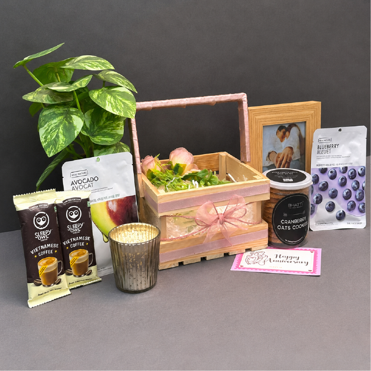 Gift basket with coffee packets, a plant, a candle, and a photo frame on a gray surface.