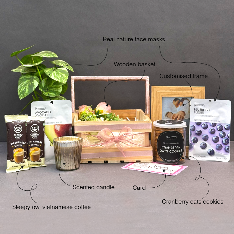 Gifting set with wooden basket, coffee packages, cookies, candle, and photo frame on a gray background