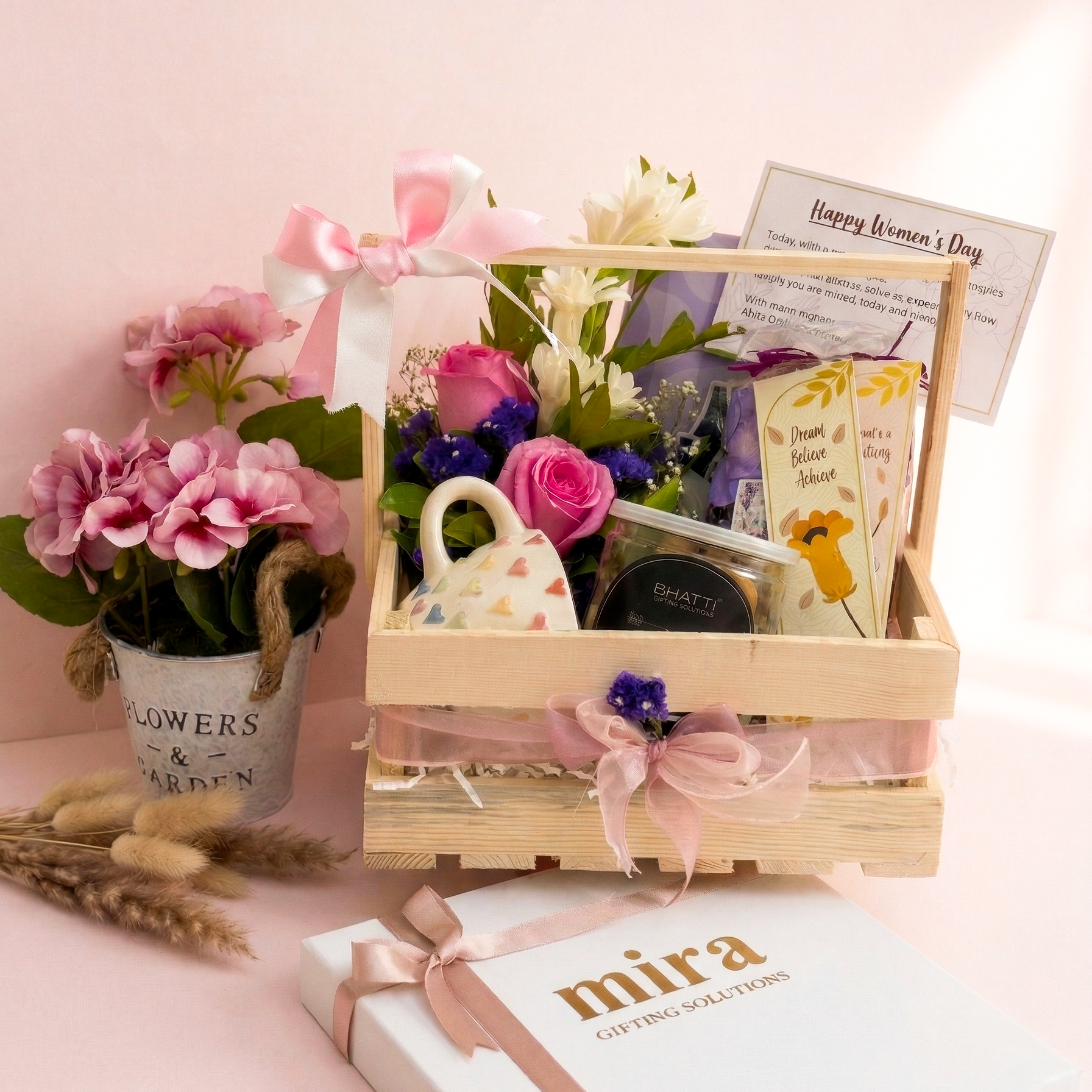 Gift basket with flowers, tea set, and cards on a pink background