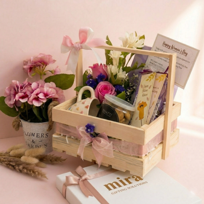 Gift basket with flowers, mug, and snacks on a pink background