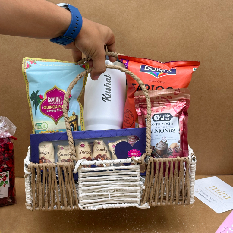 Hand holding a gift basket with snacks and a mug against a brown background