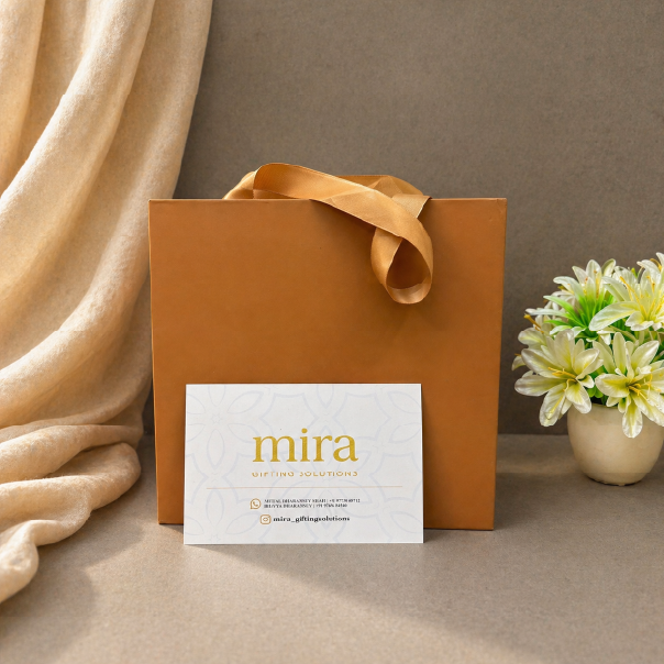 Brown gift bag with a 'mira' card on a beige surface with flowers in the background