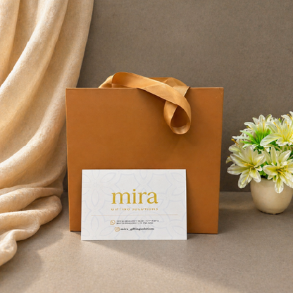 Brown gift bag with a 'mira' card on a beige surface with flowers in the background