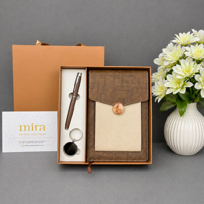 Gift set with pen, notebook, and keychain in a box on a gray background with flowers.