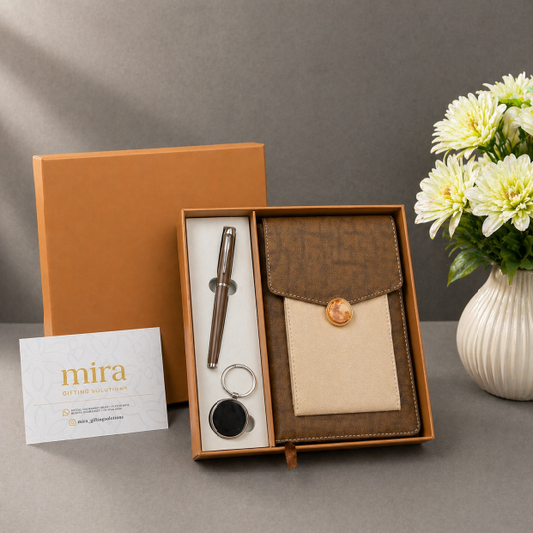 Gift set with pen, case, and keychain in a box on a gray surface with a vase of flowers in the background.