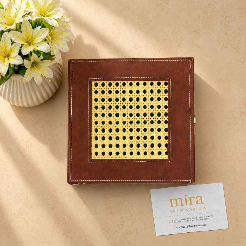 Brown leather box with gold pattern on a beige surface, accompanied by a 'mira' card.