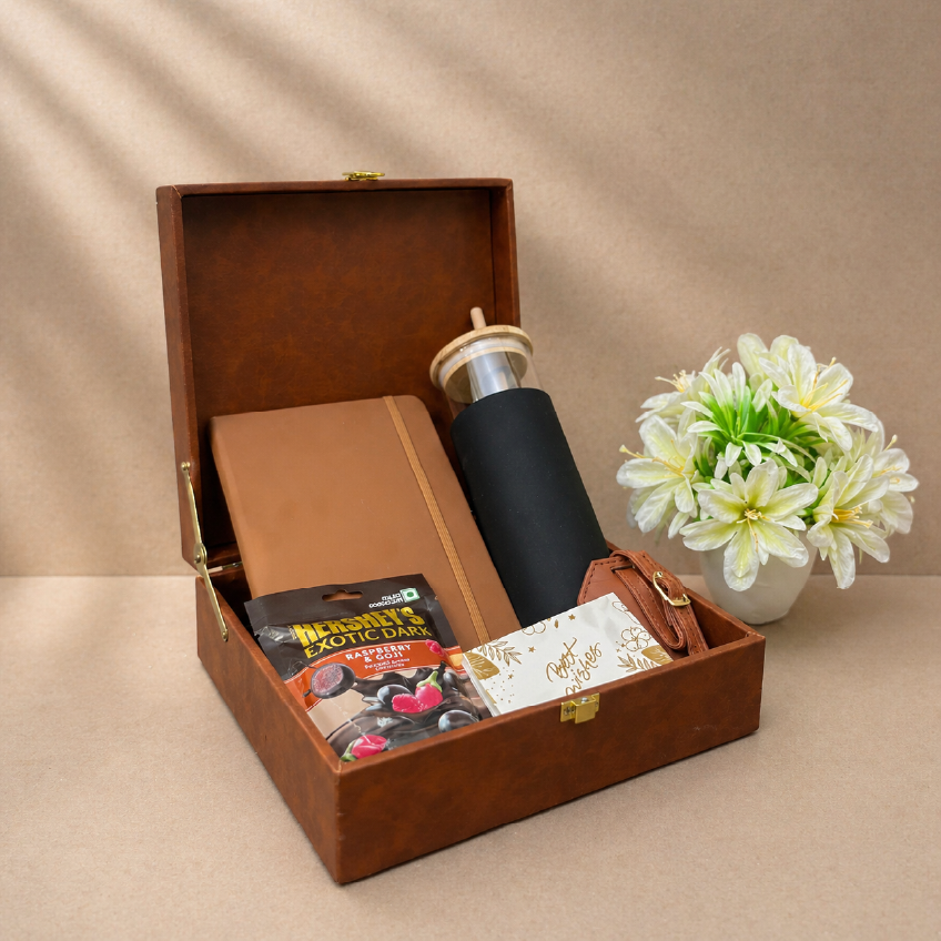 Brown gift box with a black mug, chocolate bars, and a card on a beige background