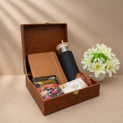 Brown gift box with a black mug, chocolate bars, and a card on a beige background