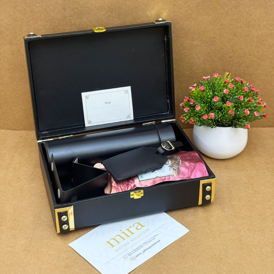 Black leather case with gold accents containing a bottle and accessories, on a brown surface with a plant in the background.
