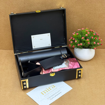 Black leather case with gold accents containing a bottle and accessories, on a brown surface with a plant in the background.