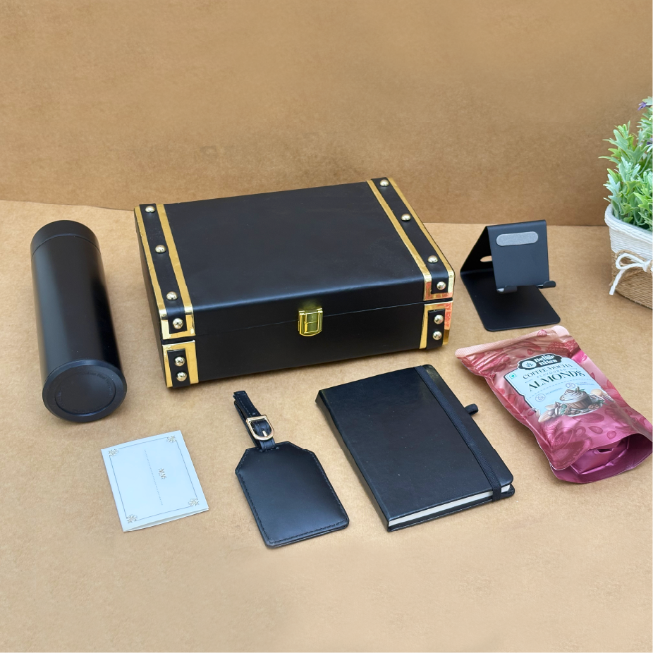 Collection of black leather items including a box, notebook, tag, and pen holder on a beige surface.