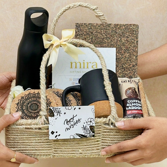 Gift basket with black mug, water bottle, and other items held by hands against a neutral background