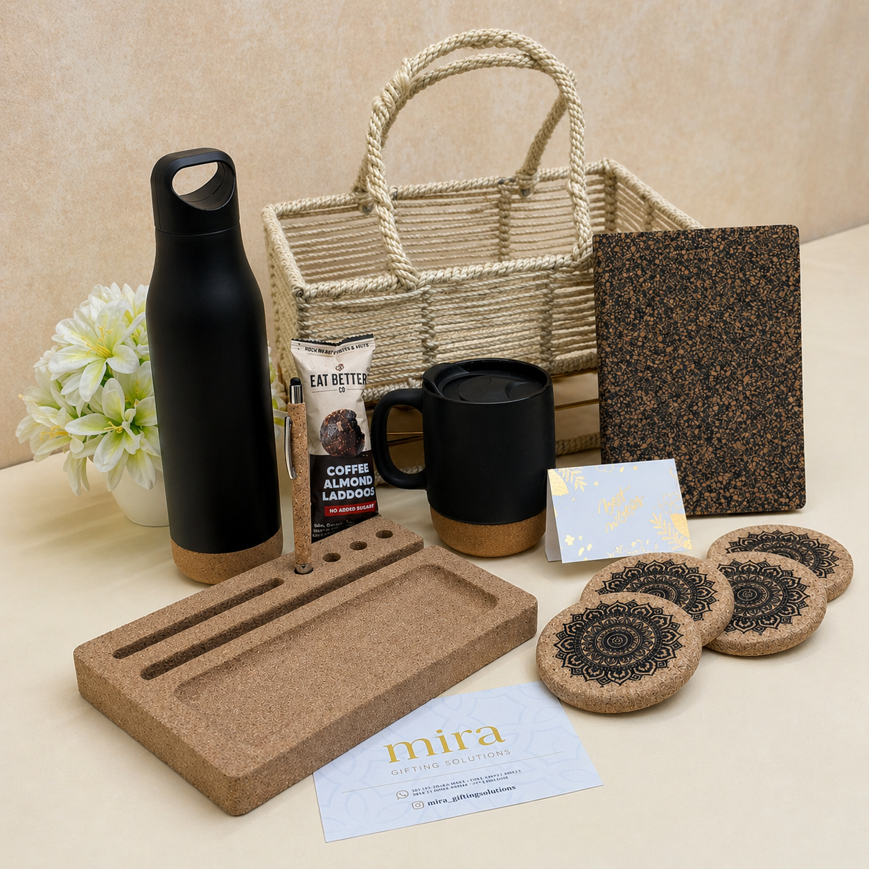 Collection of eco-friendly products including a bottle, jute basket, cork diary, printed coasters, ceramic mug, pen, and laddoo on a light background.