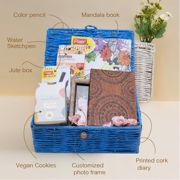 Gift basket with stationery items including a mandala book, water sketchpen, vegan cookies, and a printed cork diary on a beige background.