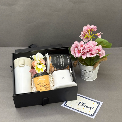 Gift set with coffee cups, thermos, and flowers on a gray surface