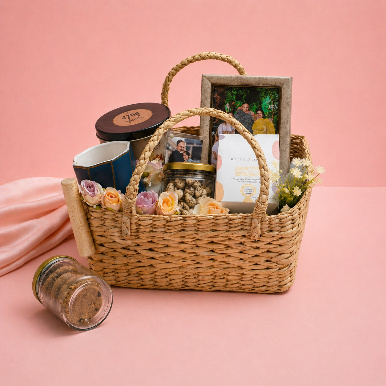 Wicker gift basket with flowers, mugs, and a photo album on a pink background