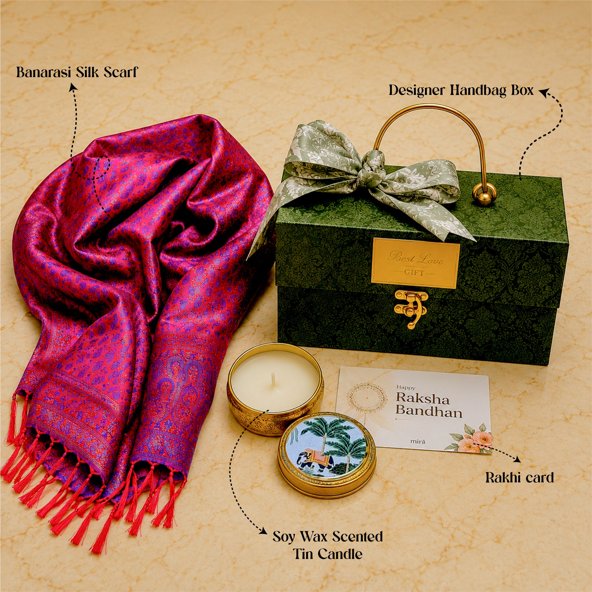 A curated gift set on a beige textured background featuring a magenta and purple Banarasi silk scarf, a dark green designer handbag box with a gold handle, a soy wax scented tin candle, and a Rakhi card with handwritten text.