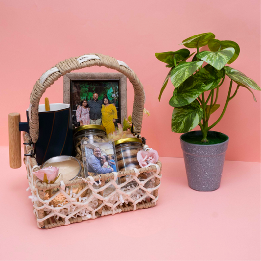 Wicker basket with jars, a mug, and a photo frame on a pink background with a plant.