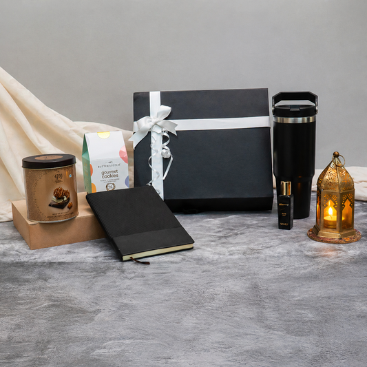Gift set with a black notebook, candle, and other items on a gray surface.