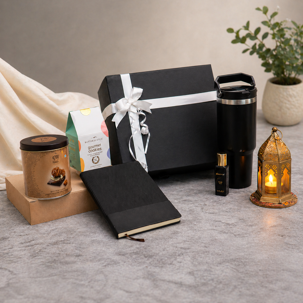 Gifting set with black gift box, notebook, candle, and other items on a gray surface.