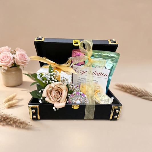 Gift set in a black suitcase with flowers, jewelry, and a card on a beige background