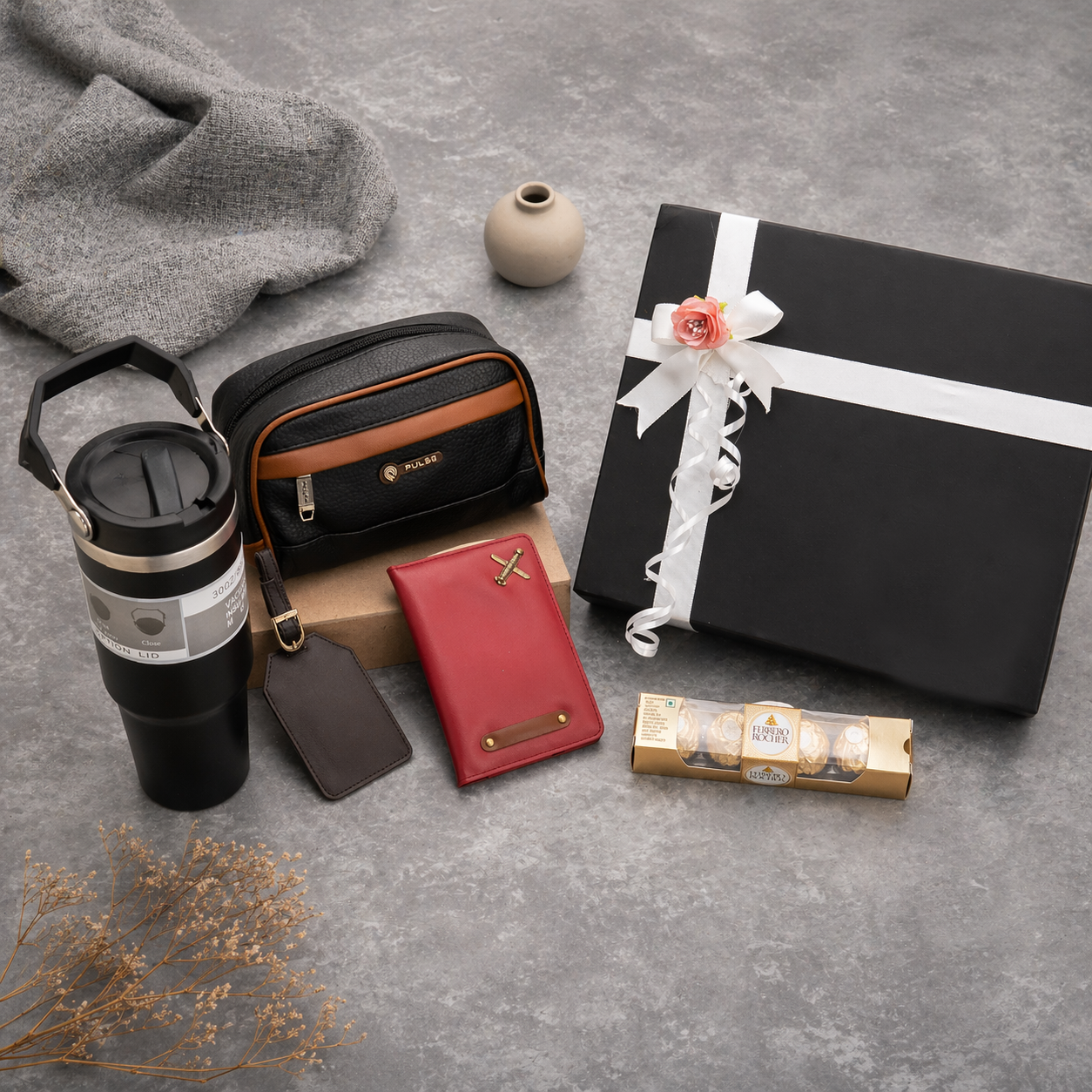 Collection of travel and gift items including a tumbler, wallet, and wrapped gift on a gray surface.