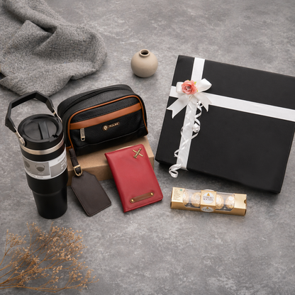 Collection of travel and gift items including a tumbler, wallet, and wrapped gift on a gray surface.