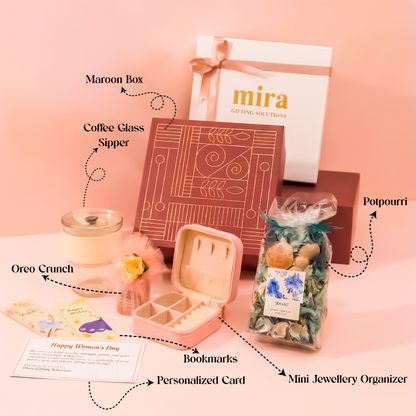 Gifting set with maroon box, coffee glass sipper, oreo crunch, potpourri, personalized card, bookmarks, and mini jewelry organizer on a pink background.