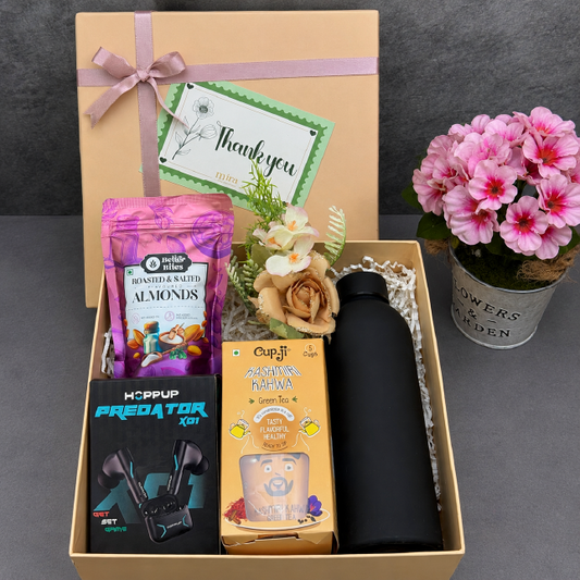Gift box with snacks, a water bottle, and a small plant on a dark surface.