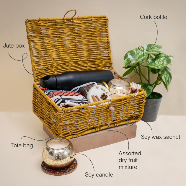 Wicker basket with labeled items including a cork bottle, tote bag, soy candle, and assorted dry fruit mixture.